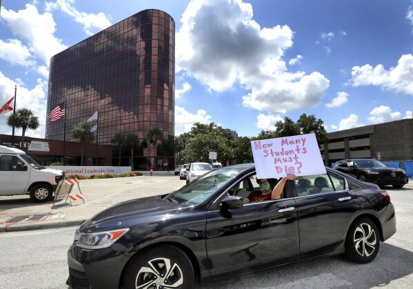 FILE - In this July 7, 2020, file photo, a teacher holds up a sign while driving by the Orange County Public Schools headquarters as educators protest in a car parade around the administration center in downtown Orlando, Fla. As the Trump administration pushes full steam ahead to force schools to resume in-person education, public health experts warn that a one-size-fits-all reopening could drive infection and death rates even higher. (Joe Burbank/Orlando Sentinel via AP, File)