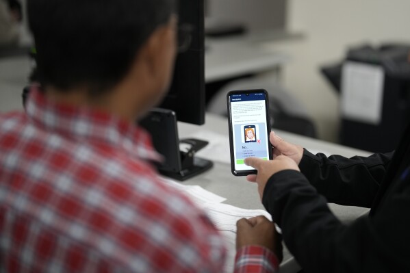 FILE - An officer helps set up a phone that will be used to track a man at an immigration and customs processing facility on March 15, 2023, in San Diego. U.S. authorities are sharply expanding the reach of curfews for the heads of asylum-seeking families while they wait for initial screenings after crossing the border, signaling they are comfortable with early results of what is intended as an alternative to detention. (AP Photo/Gregory Bull, File)