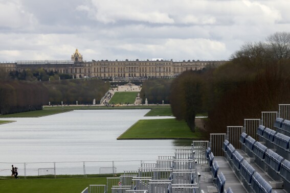 A couple jogs past the stands to watch the equestrian sports, Friday, March 29, 2024 in the park of the Chateau de Versailles, west of Paris. The site will be the venue for equestrian sports at the Paris 2024 Olympic Games. The Chateau de Versailles is seen in background. (AP Photo/Thomas Padilla)