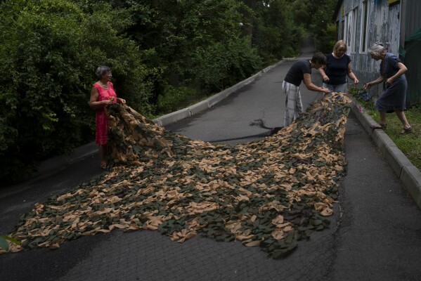 FILE - A group of church members work on a camouflage net to ship it to the frontlines in Kyiv, Ukraine, Wednesday, July 26, 2023, as the country's war against Russia continues. Life in the capital of a war-torn country seems normal on the surface. In the mornings, people rush to their work holding cups of coffee. Streets are filled with cars, and in the evenings restaurants are packed. But the details tell another story. (AP Photo/Jae C. Hong, File)