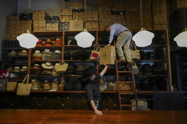 Employees work together to store products on a top shelf at the “Donde Golpea el Monito” hat shop and museum that preserves a hat-making tradition dating back to 1915, in Santiago, Chile, Thursday, April 3, 2025. (AP Photo/Esteban Felix)