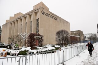 FILE - In this  Monday, Feb. 11, 2019 file photo, a woman passes by the Tree of Life Synagogue in Pittsburgh's Squirrel Hill neighborhood. Leaders of the synagogue where worshippers were fatally shot last year want to rebuild and renovate the building, turning it into what they hope will be a symbol against hatred and “the center for Jewish life in the United States.” On Thursday, Oct. 17, 2019 they outlined their vision for the Tree of Life building, where three congregations — Tree of Life, Dor Hadash and New Light — had gathered Oct. 27 when a gunman opened fire, killing 11 and wounding seven.. (AP Photo/Keith Srakocic, File)