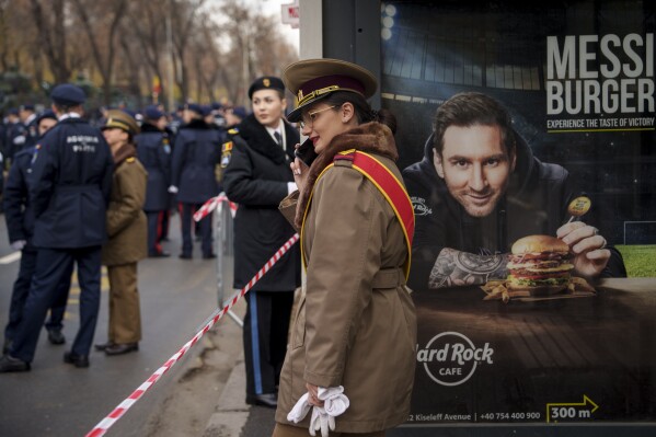 A military cadet speaks on the phone backdropped by a billboard showing Argentinian soccer star Lionel Messi in Bucharest, Romania, Friday, Dec. 1, 2023. Tens of thousands of people turned out in Romania's capital on Friday to watch a military parade that included troops from NATO allies to mark the country's National Day(AP Photo/Vadim Ghirda)