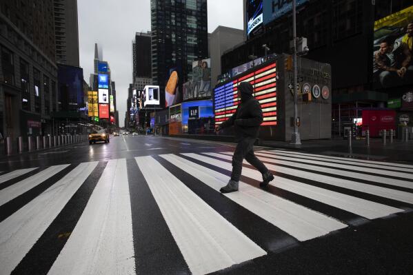 FILE - A man crosses the street in a nearly empty Times Square, which is usually very crowded on a weekday morning in New York on March 23, 2020. (AP Photo/Mark Lennihan, File)