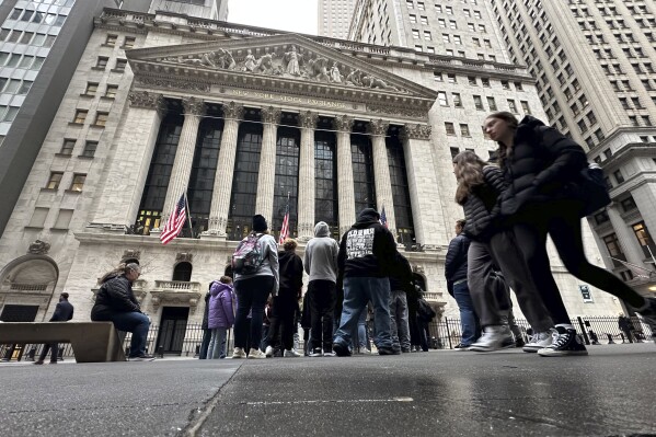FILE - People walk past the New York Stock Exchange March 27, 2024. Global shares are trading higher on Monday, April 29, 2024, amid optimism over the rally that ended the week on Wall Street, although eyes are on the Federal Reserve policy meeting set for later this week. (AP Photo/Peter Morgan, File)