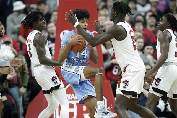 North Carolina guard Puff Johnson (14) grabs a rebound against North Carolina State guard Dereon Seabron (1) and forward Ebenezer Dowuona, right, during the second half of an NCAA college basketball game in Raleigh, N.C., Saturday, Feb. 26, 2022. (AP Photo/Gerry Broome)
