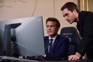 FILE - French President Emmanuel Macron plays a video game next to Adrien Nougaret, aka ZeratoR, during a meeting with French esport video game players at the Elysee Palace in Paris, Friday June 3, 2022. French President Emmanuel Macron is extending an olive branch to video gamers after previously linking video games to riots that rocked France this year. Posting on the platform previously known as Twitter, Macron backpedalled on remarks where he had blamed video games for having “intoxicated” some young rioters. (Julien de Rosa, Pool via AP, File)