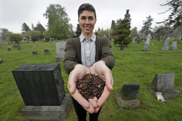 FILE - In this April 19, 2019, file photo, Katrina Spade, the founder and CEO of Recompose, a company that hopes to use composting as an alternative to burying or cremating human remains, poses for a photo in a cemetery in Seattle, as she displays a sample of compost material left from the decomposition of a cow using a combination of wood chips, alfalfa and straw. (AP Photo/Elaine Thompson, File)