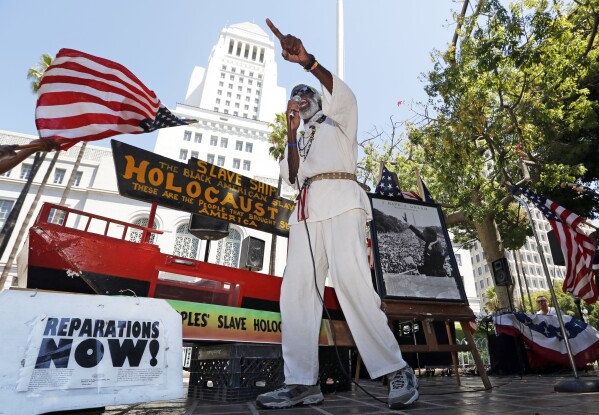 FILE - Los Angeles activist Ted Hayes stands with a scale model of a slave ship, in which thousands of slaves were brought to North America, during a rally to commemorate the 50th anniversary of the March On Washington, at Los Angeles City Hall Wednesday, Aug. 28, 2013. Hayes emphasized the part of the Rev. Martin Luther King's 1963 "I Have A Dream" speech that called for reparations for the descendants of those involuntarily brought from Africa to what later became the United States. (AP Photo/Reed Saxon, File)