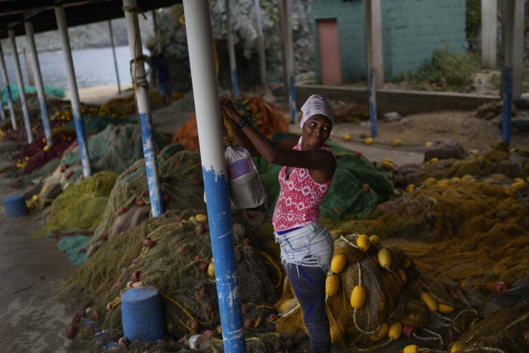 Fisherwoman Ana Ache unhooks her bag above fishing nets as she prepare to return home after a day of fishing in Chuao, Aragua state, Venezuela, Tuesday, June 6, 2023. Chuao is also the source of Venezuela’s most prized cacao, the raw ingredient in chocolate. But like other industries, chocolate has experienced a decline since the country’s crisis began last decade, pushing more people into fishing. (AP Photo/Matias Delacroix)