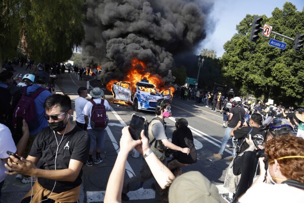 People watch while several Waymo cars burn in downtown Los Angeles after being vandalized by protesters reacting to a series of immigration raids that occurred in Los Angeles, Calif., on Sunday, June 8, 2025. (Stephen Lam/San Francisco Chronicle via AP)