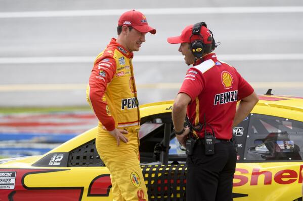 Joey Logano, left, talks with a team member as his car sits parked on pit row during a rain delay of a NASCAR Cup series auto race Monday, Oct. 4, 2021, in Talladega, Ala. (AP Photo/John Amis)