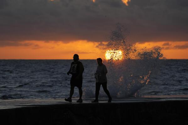 FILE - The sun rises above the Atlantic Ocean as waves crash near beach goers walking along a jetty, Dec. 7, 2022, in Bal Harbour, Fla. The world's oceans have suddenly spiked much hotter and well above record levels, with scientists trying to figure out what it means and whether it forecasts a surge in atmospheric warming. (AP Photo/Wilfredo Lee, File)