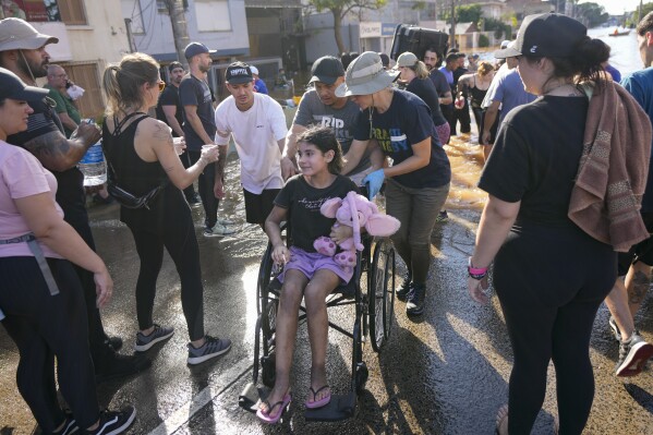 Freiwillige schieben am Dienstag, den 7. Mai 2024, einen Rollstuhl, um einen Evakuierten aus einem von starkem Regen überschwemmten Gebiet in Porto Alegre, Brasilien, zu transportieren. (AP Photo/Andre Penner)