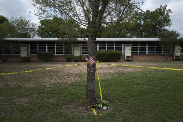 A school building stands behind a tree with an American flag and crime scene tape at Robb Elementary School in Uvalde, Texas Monday, May 30, 2022. On May 24, 2022, an 18-year-old entered the school and fatally shot several children and teachers. (AP Photo/Jae C. Hong)