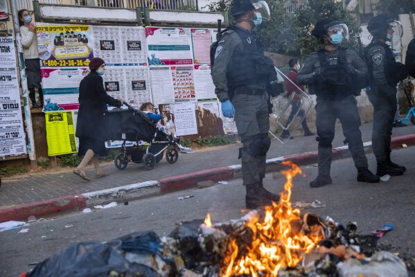 Israeli police officers stand by burning garbage during clashes with ultra-Orthodox Jews over the coronavirus lockdown restrictions, in Bnei Brak, Israel, Sunday, Jan. 24, 2021. As he seeks re-election, Prime Minister Benjamin Netanyahu has turned to a straightforward strategy: Count on the rock-solid support of his ultra-Orthodox political allies and stamp out the coronavirus pandemic with one of the world’s most aggressive vaccination campaigns. But with ultra-Orthodox communities openly flouting safety guidelines and violently clashing with police trying to enforce them, this marriage of convenience is turning into a burden. (AP Photo/Oded Balilty)