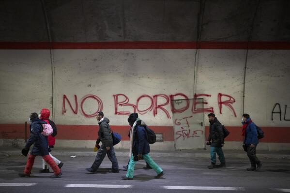 Migrants headed to France from Italy walk by a grafitti that reads "No Border" in a tunnel leading to the French-Italian border, Saturday, Dec. 11, 2021. As Europe erects ever more fearsome barriers against migration, volunteers along the Italy-France border are working to keep migrants from being killed or maimed by cold and mountain mishaps as they cross the high Alps. (AP Photo/Daniel Cole)
