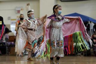 In this photo provided by the American Indian Child Resource Center, Native American children dance while wearing masks at a powwow hosted by the American Indian Child Resource Center featuring traditional Native American music and dancing, along with the chance to get COVID-19 vaccinations and testing, on Dec. 4, 2021, at La Escuelita Elementary School, in Oakland, Calif.  (Garrett Rich/American Indian Child Resource Center via AP)