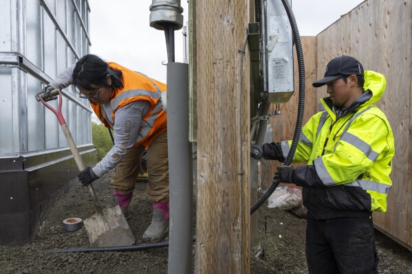 Alaska Native Tribal Health Consortium staff Darlene Ayapan, left, uses a shovel as Terrance Ekamrak installs a power supply cable to a newly developed lift house, Thursday, Aug. 17, 2023, in Akiachak, Alaska. (AP Photo/Tom Brenner)