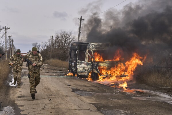 In this photo provided by the Ukrainian 10th Mountain Assault Brigade "Edelweiss", Ukrainian soldiers pass by a volunteer bus burning after a Russian drone hit it near Bakhmut, Donetsk region, Ukraine, Thursday, Nov. 23, 2023. (Shandyba Mykyta, Ukrainian 10th Mountain Assault Brigade "Edelweiss" via AP)