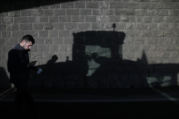 FILE - A farmer checks his mobile phone as his tractor casts a shadow under a closed highway bridge in Chilly-Mazarin, south of Paris, on Wednesday, January 31, 2024. French farmers continued to protest around Paris and on major roads across the country on Wednesday as police were called in to protect the capital, airports and international markets.  (AP Photo/Christoph Ena, File)