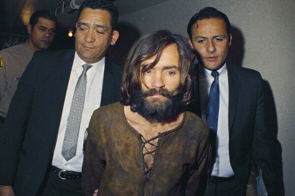 
              FILE - In this 1969 file photo, Charles Manson is escorted to his arraignment on conspiracy-murder charges in connection with the Sharon Tate murder case. Authorities say Manson, cult leader and mastermind behind 1969 deaths of actress Sharon Tate and several others, died on Sunday, Nov. 19, 2017. He was 83. (AP Photo, File)
            