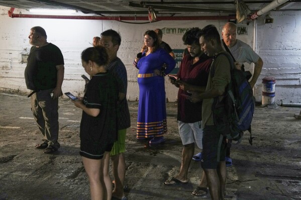 Residents check their cell phones at a shelter during an alarm for incoming missiles launched from Iran in Haifa, Israel, Sunday, June 22, 2025. (AP Photo/Baz Ratner)