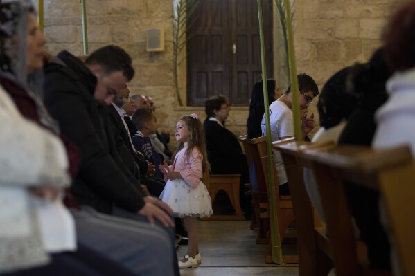 A girl holds a candle as worshippers pray during Palm Sunday Mass at the Maronite Church of St. George in Quraye, near the southern port city of Sidon, Lebanon, Sunday, April 13, 2025. The service marked the traditional Palm Sunday procession. (AP Photo/Hassan Ammar)