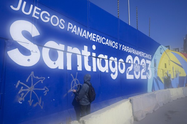A demonstrator paints graffiti on a billboard advertising the Santiago 2023 Pan American Games, during protests marking the fourth anniversary of anti-government protests, in Santiago, Chile, Wednesday, Oct. 18, 2023. The opening ceremony for the XIX Pan American Games will take place in Santiago on Oct. 20. (AP Photo/Esteban Felix)