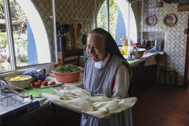 Nun Maria Ines Maldonado, 76, carries a tray of corn husks stuffed with shredded chicken and salsa verde at the Convent of the Mothers Perpetual Adorers of the Blessed Sacrament in Mexico City, Friday, Dec. 1, 2023. (AP Photo/Ginnette Riquelme)