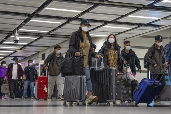 FILE - Travelers wearing face masks with their luggage head to the immigration counter at the departure hall at Lok Ma Chau station following the reopening of crossing border with mainland China, in Hong Kong, Sunday, Jan. 8, 2023. Hong Kong authorities announced Friday, Feb. 3, 2023, that they will lift a quota on the number of cross-border travelers with China and scrap mandatory COVID-19 PCR testing requirements as both places seek to drive economic growth. (AP Photo/Bertha Wang, File)