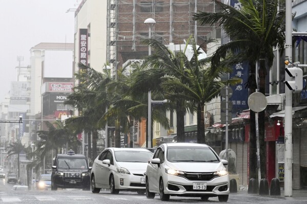 Vehicles drive through a street in a strong wind in Naha, Okinawa prefecture, southern Japan Sunday, Aug. 6, 2023. A meandering storm was headed again toward southwestern Japan on Sunday, prompting fresh warnings about dangerously heavy rainfall after the same area was hit several days ago. (Kyodo News via AP)