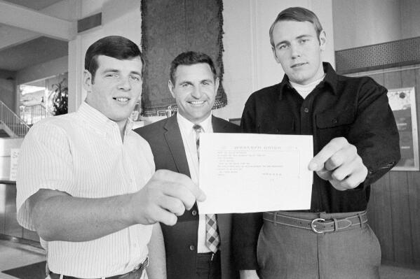 University of Arizona football coach Darrell Mudra is flanked by his two quarterbacks, Mark Driscoll, left and Bruce Lee as they hold a copy of telegram from Apollo 8 commander Col. Frank Borman, an Arizona native, on Dec. 28, 1968, in El Paso, Texas. The telegram was sent to the team in El Paso by Borman's wife, Sue Borman, an alumni of Arizona, wishing them well in their Sun Bowl game with Auburn University. Mudra, a College Football Hall of Fame coach, who won better than 70% of his games and two national championships in a career spanning the 1950s through 1980s, died Wednesday, Sept. 22, 2022, The National Football Foundation said. He was 93. (AP Photo/Ferd Kaufman)