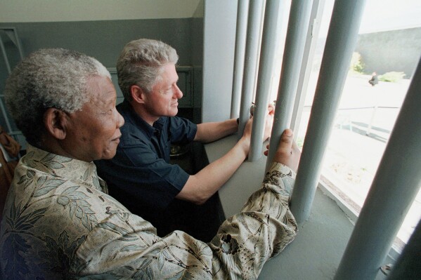 FILE - Nelson Mandela, left, and former US president Bill Clinton look to the outside from Mandela's Robben Island prison cell in Cape Town, South Africa, March 27, 1998. The South African government announced Friday Jan. 19, 2024 that it plans to challenge an auction of artifacts which belonged to Mandela, set to take place in New York next month. (AP Photo/Scott Applewhite, Pool, File)
