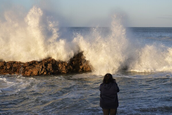 A woman photographs big waves in Port Elizabeth, South Africa, Sunday, Sept. 17, 2023. South African authorities say big ocean waves caused by a phenomenon known as "spring tide" crashed into coastal parts of the country over the weekend, leaving two people dead and injuring several. (AP Photo Deon Ferreira)