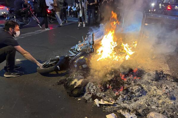 In this Monday, Sept. 19, 2022, photo taken by an individual not employed by the Associated Press and obtained by the AP outside Iran, a man pulls out a police motorcycle which is set on fire during a protest over the death of a young woman who had been detained for violating the country's conservative dress code, in downtown Tehran, Iran. (AP Photo)