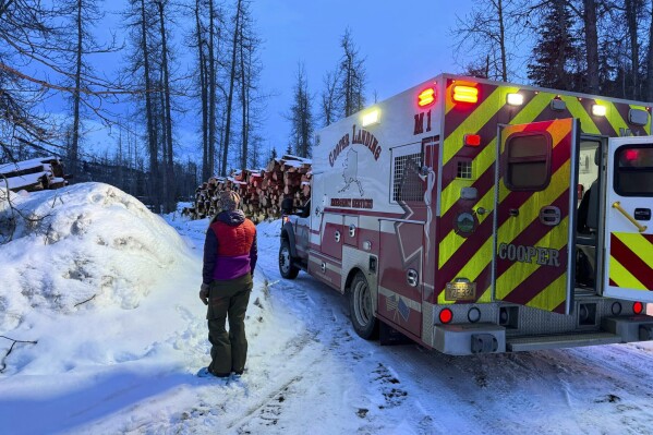 In this image provided by the Cooper Landing Emergency Services, a member of the Cooper Landing EMS rescuers looks at the mountain to see if troopers are bringing down avalanche survivors on Tuesday, Feb. 13, 2024, in Cooper Landing, Alaska. One backcountry skier died and two others were injured in an avalanche on Alaska's Kenai Peninsula, as warm weather raises the risk for such events in the state. (Clay Adam/Cooper Landing Emergency Services via AP)