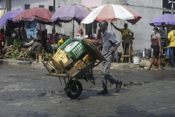 A man pushes a wheelbarrow, at a market in Lagos, Nigeria, Thursday Dec. 24, 2020. Africa’s top public health official says another new variant of the coronavirus appears to have emerged in Nigeria, but further investigation is needed. The discovery could add to new alarm in the pandemic after similar variants were announced in recent days in Britain and South Africa and sparked the swift return of travel restrictions. (AP Photo/Sunday Alamba)