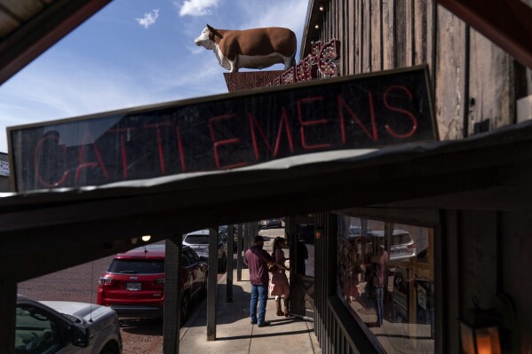 A bull statue stands atop a steakhouse restaurant as a couple walk in for dinner in Forth Worth, Texas, Friday, April 21, 2023. For much of the nation's history, beef has been a staple of Americana, with baying cattle given starring roles in Westerns, Big Macs and Whoppers drawing long lines at drive-up windows and a filet mignon the highlight of a celebratory meal. (AP Photo/David Goldman)