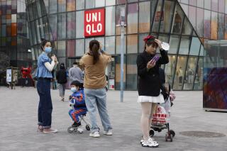FILE - In this Monday, March 29, 2021 file photo, visitors to a shopping mall wearing masks stand before a Uniqlo store in Beijing. French prosecutors have on Friday, July 2 opened an investigation into alleged involvement in crimes against humanity based on accusations that global retailers, including Uniqlo and the makers of Skechers shoes and Zara clothes, rely on forced labor of minorities in China. (AP Photo/Ng Han Guan)