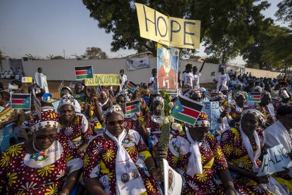 FILE - Women holding national flags and peace banners await the arrival of Pope Francis at the St. Theresa Cathedral in Juba, South Sudan on Feb. 4, 2023. As South Sudan’s plans to hold its first elections in December that should signify a major milestone in efforts to get lasting peace since the end of the civil war, mass violence and accompanying gross human rights violations continue unabated, a report by the UN Commission on Human Rights in South Sudan says. (AP Photo/Ben Curtis, File)