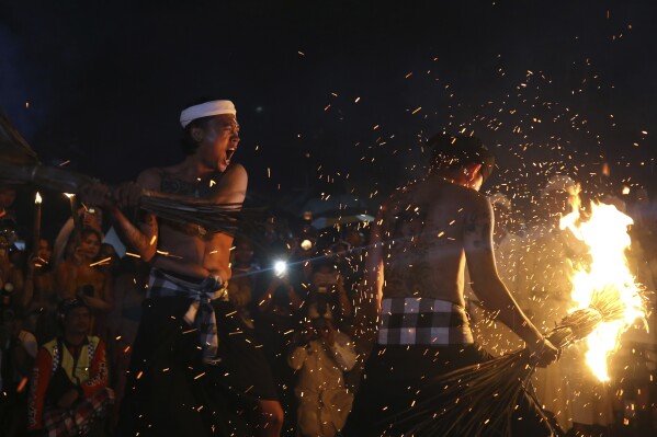 A Hindu devout hits another with burning coconut leaves, sending sparks and embers flying in all directions, in a ritual known as Lukat Gni, as part of Balinese Hindu New Year celebrations, in Bali, Indonesia on Sunday, March 10, 2024. (AP Photo/Firdia Lisnawati)