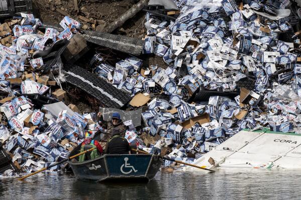 A group of fishermen claim a bottle of beer from a derailed railcar on the banks of the Clark Fork River near Quinn's Hot Springs, west of St. Regis, Mont., Sunday, April 2, 2023. Montana Rail Link is investigating the derailment in which there were no injuries reported. (Ben Allan Smith/The Missoulian via AP)