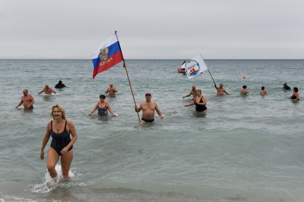 FILE - Crimean people wave a Russian national flag celebrating an Orthodox Christmas in the Black Sea in Yevpatoria, Crimea, Thursday, Jan. 7, 2016. The Crimean Peninsula's balmy beaches have been vacation spots for Russian czars and has hosted history-shaking meetings of world leaders. And it has been the site of ethnic persecutions, forced deportations and political repression. Now, as Russia’s war in Ukraine enters its 18th month, the Black Sea peninsula is again both a playground and a battleground. (AP Photo, File)