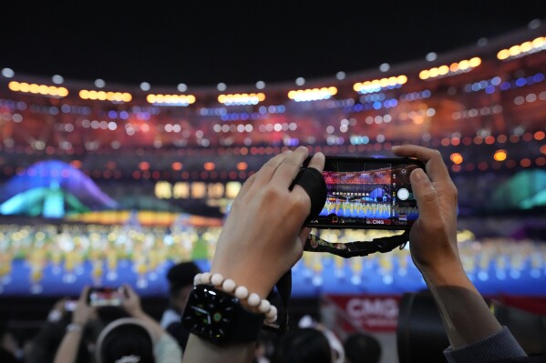 A spectator take photos of the closing ceremony of the 19th Asian Games in Hangzhou, China, Sunday, Oct. 8, 2023. (AP Photo/Eugene Hoshiko)