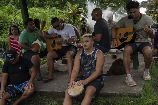 A group play music together by the side of the road in Teahupo'o, Tahiti, French Polynesia, Tuesday, Jan. 16, 2024. (AP Photo/Daniel Cole)