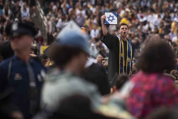 Absolwent trzyma czapkę z izraelską flagą podczas demonstracji propalestyńskich demonstrantów podczas ceremonii rozpoczęcia wiosny 2024 na Uniwersytecie Michigan na stadionie Michigan w Ann Arbor w stanie Michigan, sobota, 4 maja 2024 r.  (Raport za pośrednictwem Katie Guilty/Detroit AP)