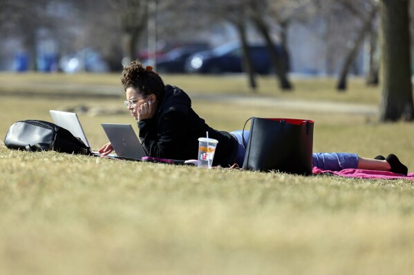 Tania Sepulveda takes advantage of the warmer than normal temperatures to work on her laptop computer outside her home near Montrose Harbor, Monday, Feb. 26, 2024, in Chicago. A warm front is sweeping spring-like weather across a large swath of the country in what is usually one of the coldest months of the year. The rare warmup is sending people out of their homes to enjoy the winter respite. (AP Photo/Teresa Crawford)