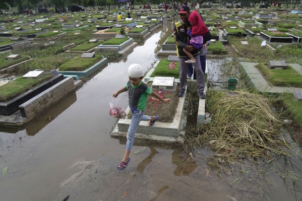 A family navigates puddles in a flooded cemetery while visiting a relative's grave ahead of the holy Muslim fasting month of Ramadan in Jakarta, Indonesia, Friday, March 8, 2024. Before Ramadan, the holiest month in the Islamic calendar , Indonesian Muslims followed the local tradition of visiting cemeteries to pray for their deceased loved ones.  (AP Photo/Dita Alangkara)
