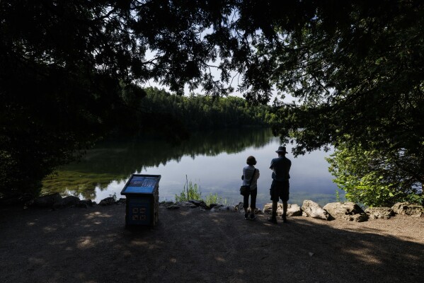 People look out at the water at Crawford Lake in Milton, Ontario, on Friday, July 7, 2023. A team of scientists is recommending the start of a new geological epoch defined by how humans have impacted the Earth should be marked at the pristine Crawford Lake outside Toronto in Canada. (Cole Burston/The Canadian Press via AP)